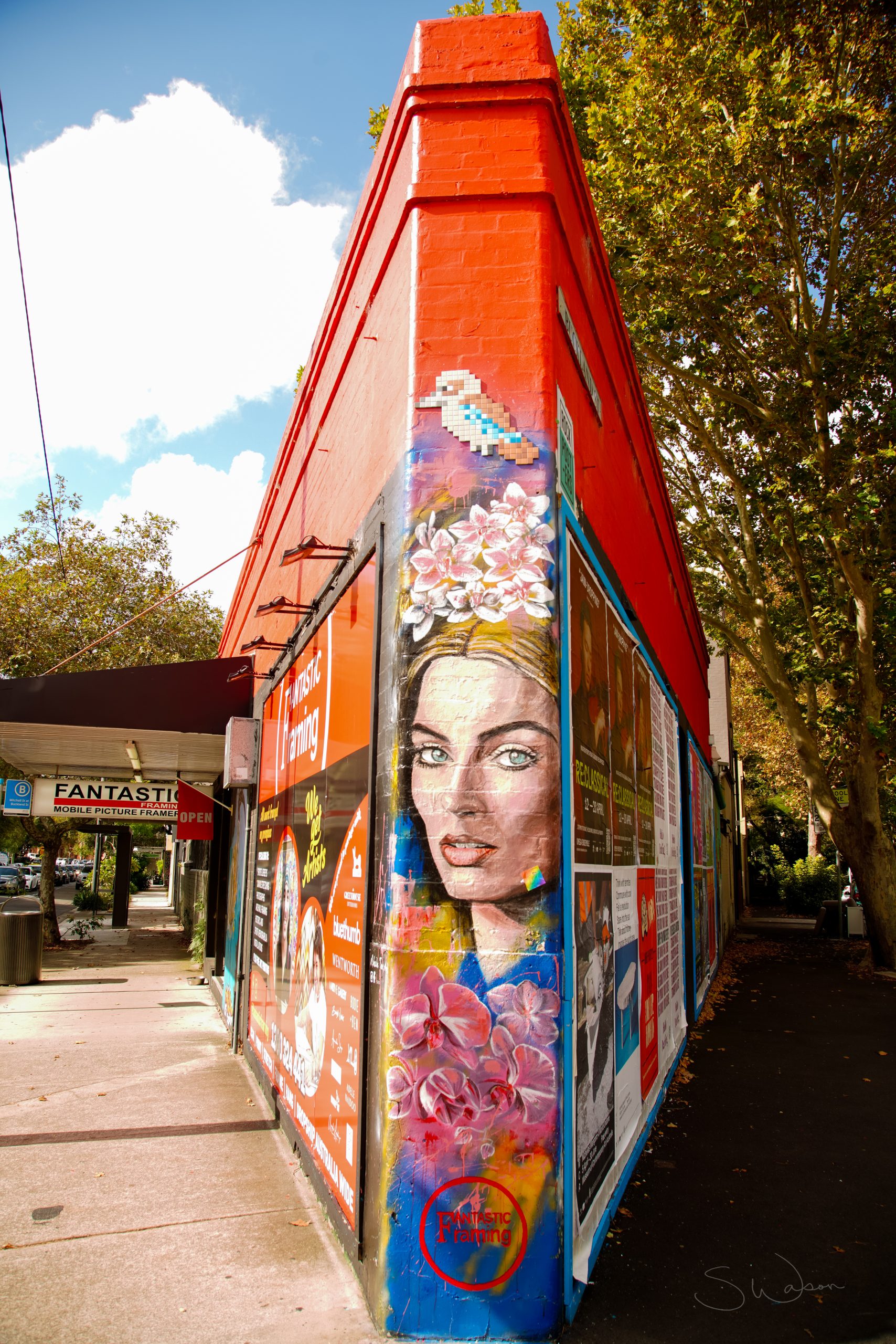 Red building coming to a point at the corner of a two streets. A woman's face is painted at the end.Travel